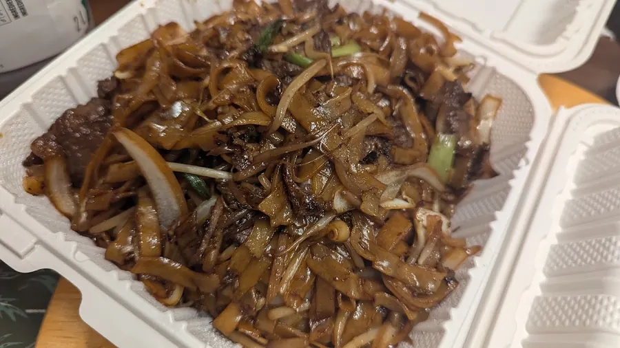 Wide rice noodles stir-fried with beef, onion and bean sprouts in a takeout box