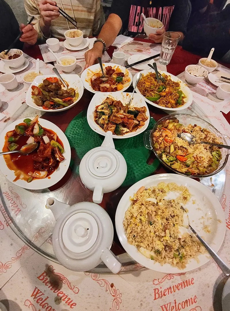 A round table with a lazy Susan full of shared dishes, fried rice, noodles and teapots