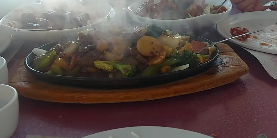 A steaming sizzling plate of beef and vegetables on a wooden board